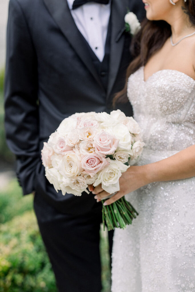 Rosecliff Mansion Wedding Photos | Brianna Graca Weddings Fine Art Wedding Photographer in Newport | Bride in sparkly gown holding bouquet of white and pink roses, standing beside groom in black suit and bow tie, conveying elegance and romance.