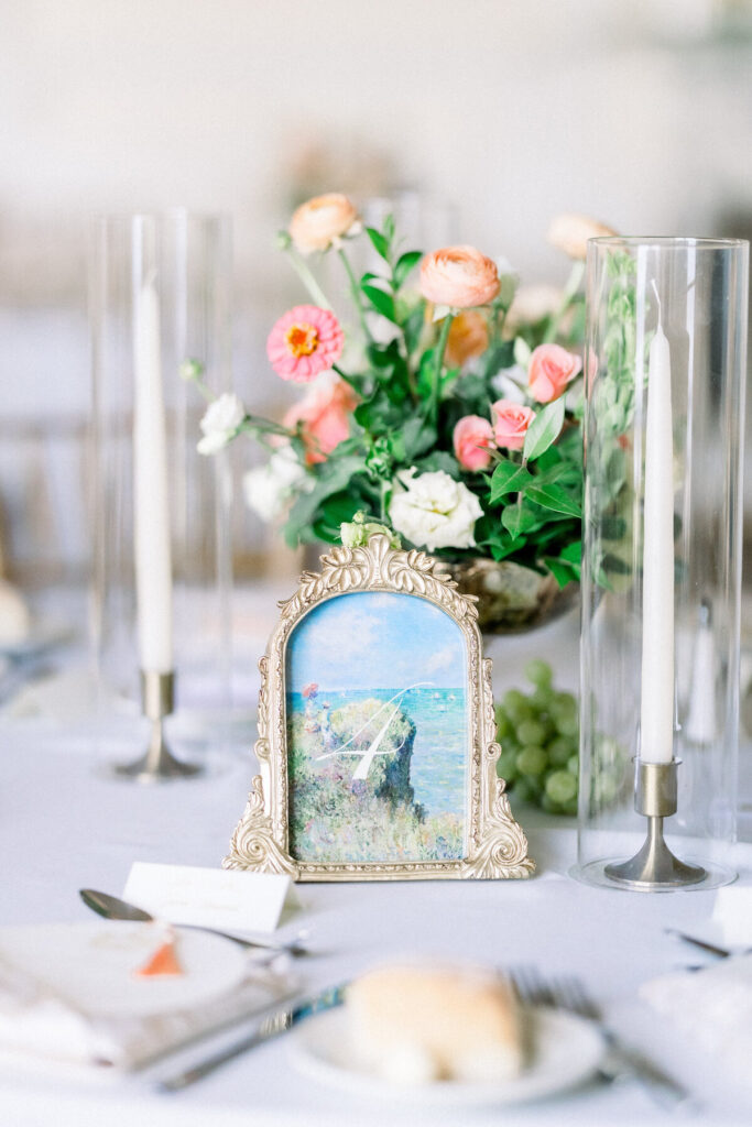 Aldrich Mansion Wedding | Brianna Graca Weddings Fine Art Wedding Photographer in Newport | Elegant table setting with a floral centerpiece of pink and white flowers, ornate picture frame showing a landscape, and tall candles in glass holders.