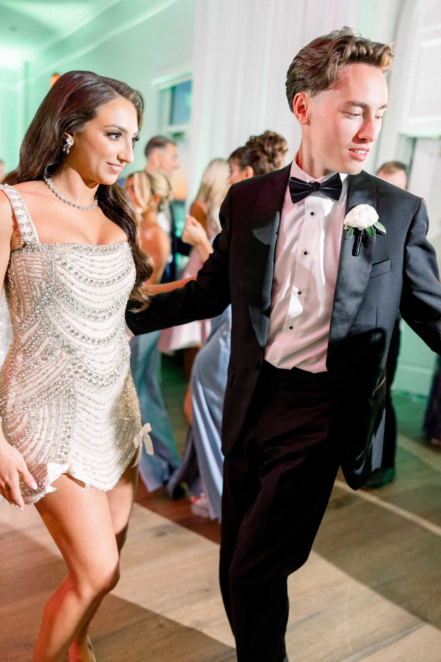 The bride dances in a beaded reception dress during her coastal black tie wedding.